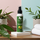 Bottle of 'Cleaner Roots' elixir on a wooden surface with plants and towels in the background.