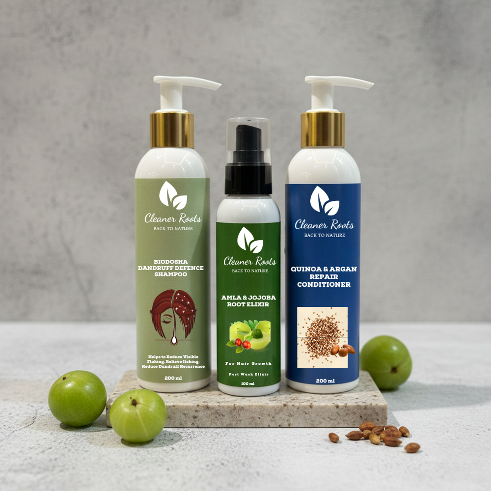 Three bottles of 'Cleaner Roots' hair care products on a stone slab with green fruits and seeds.