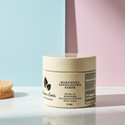 Manjistha Exfoliating Scrub jar with a brush on a light surface against a pastel background