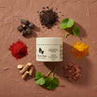 Manjistha Exfoliating Scrub container surrounded by natural ingredients on a brown textured background