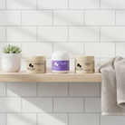 Three skincare jars on a wooden shelf with a white tiled wall background